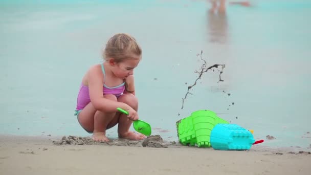 छोटी लड़की समुद्र तट पर एक रेत महल बना रही है — स्टॉक वीडियो