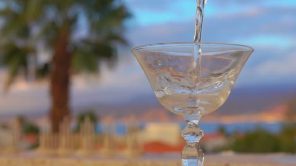 Мартини наливают в стакан на фоне моря — стоковое видео