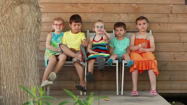 Дети сидят на стульях рядом с домом — стоковое видео