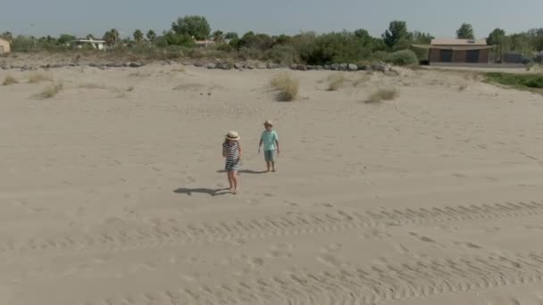 Çocuklar uçan bir dronun peşinden kumsalda koşar. — Stok video