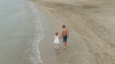 Küçük kız ve oğlan kumsalda el ele koşuyorlar.