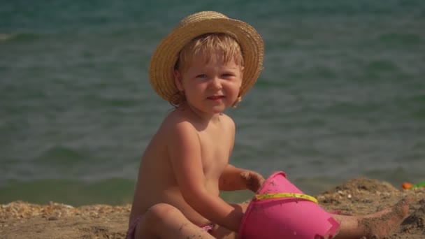 Flicka i halmhatt bygger sandslott på stranden — Stockvideo