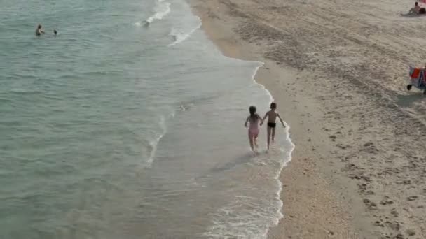 Tiro aéreo de menino e menina correndo ao longo do mar — Vídeo de Stock