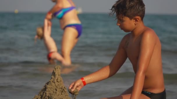 Chłopiec buduje zamek z piasku na plaży. — Wideo stockowe