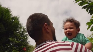 Çizgili tişörtlü baba mutlu bir çocuğu fırlatıyor.