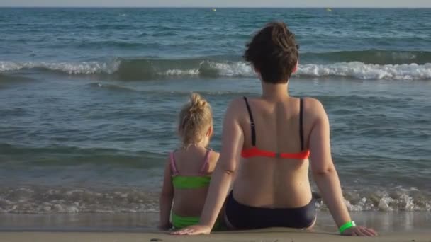 Mom and daughter sitting close together on seashore — ストック動画