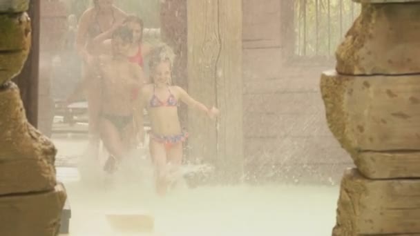 Children run through spray to slide in water park — Stock Video