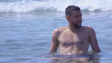 Genç yakışıklı adam denizin dalgalarında oturuyor.