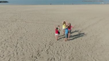 Sahilde dans eden parlak elbiseli çocuklar.