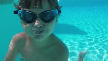 Çocuk havuza dalıyor ve komik suratlar yapıyor.