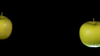 İki ıslak yeşil elma siyah zeminde çarpışıyor.