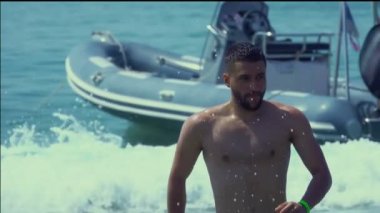Genç yakışıklı adam kameraya doğru deniz suyuyla koşuyor.
