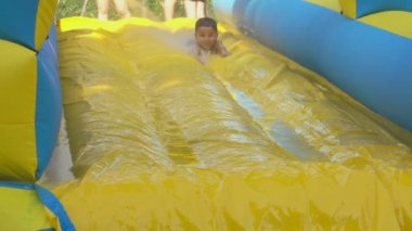 Küçük çocuk su parkında sarı köpüklü kayağa biniyor.