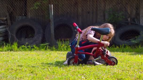 Tulumlu küçük kız bahçede bisiklet tamir ediyor. — Stok video