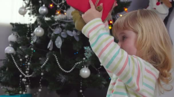 Klein schattig meisje shakes een kerstcadeau doos — Stockvideo