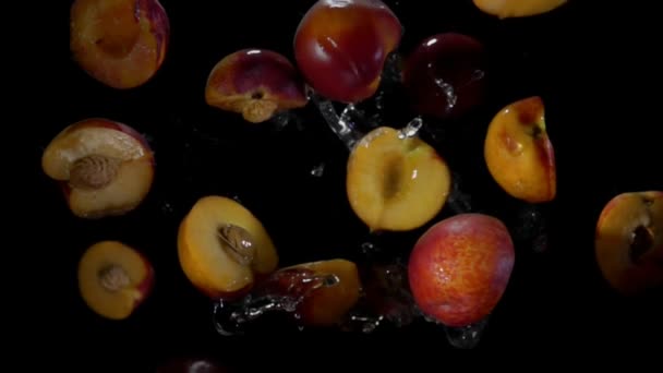 Halves of a peach fly in splashes of water — Stockvideo