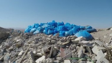 Mavi plastik torbalardaki çöpler deniz kıyısında yatıyor.
