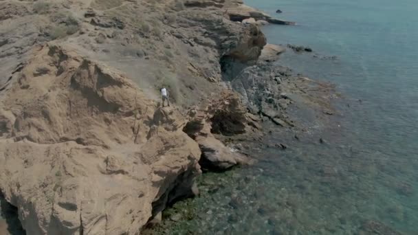 Un disparo aéreo de un hombre parado en un acantilado sobre el mar — Vídeo de stock