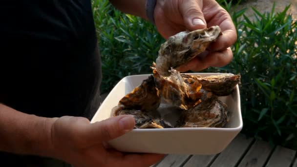 Hombre estudiando ostras frescas en un plato blanco — Vídeos de Stock