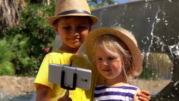 Маленький хлопчик і дівчинка в соломі роблять селфі по телефону — стокове відео