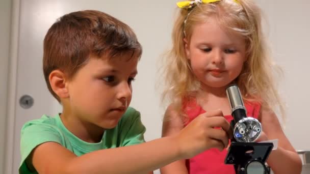 Menino ajuda uma menina a olhar através de um microscópio — Vídeo de Stock