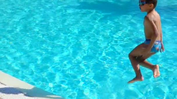 Pojken i simglasögon hoppar i poolen. — Stockvideo