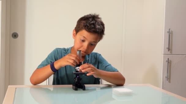 Un chico serio de ojos negros está regulando un microscopio. — Vídeos de Stock