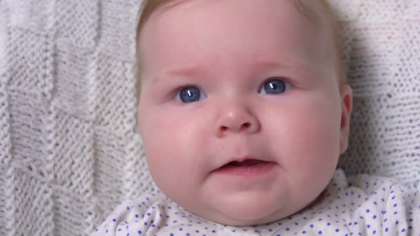 Blauwogige baby kijkt nieuwsgierig naar de camera — Stockvideo