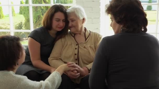 Пожилая женщина сидит на диване со своими внучками — стоковое видео