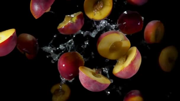 Halves of a peach fly in splashes of water — Stockvideo