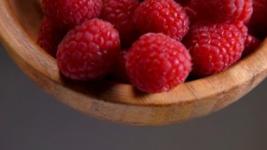 Large juicy raspberries fall out of a wooden bowl
