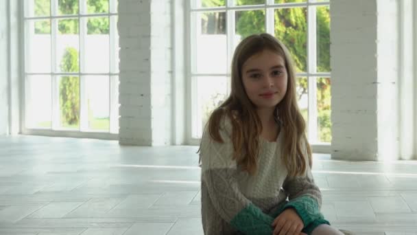 Belle fille souriante et assise dans un hall blanc ensoleillé avec de grandes fenêtres — Video