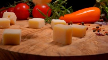 Sert peynir küpleri, baharat ve domateslerle dolu tahta bir tahtaya düşer.