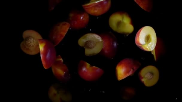 Halva persikor studsa med stänk av vatten på den svarta bakgrunden — Stockvideo