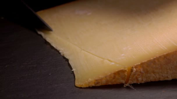 El cuchillo corta un queso duro en rodajas sobre una superficie negra — Vídeos de Stock