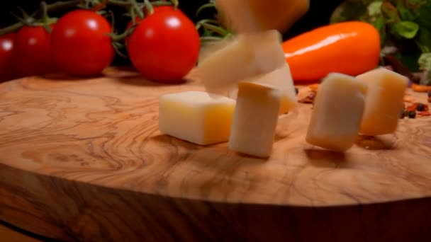 Cubos de queso duro caen en una tabla de madera con especias y tomates cherry — Vídeos de Stock