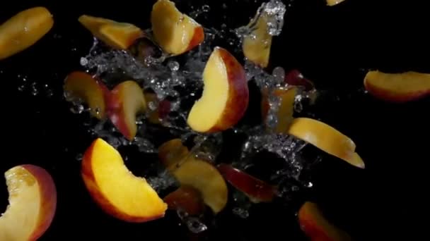 Slices of peaches are flying with splashes of water on the black background — Stock Video