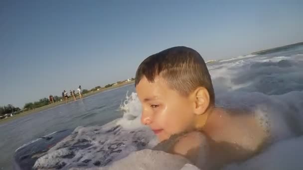 Garçon sur une planche de natation surfe sur la vague éclaboussante vers la côte — Video