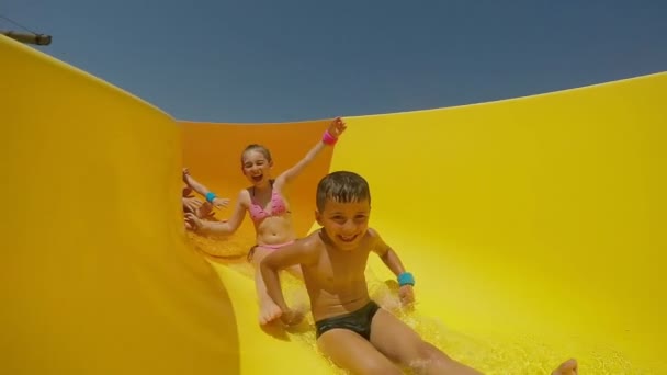 Crianças alegres estão descendo a corrediça laranja no parque aquático — Vídeo de Stock