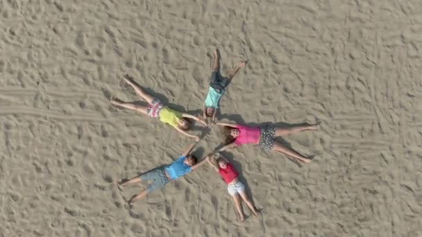 Kinderen in heldere kleren liggen op het zand in de vorm van een ster — Stockvideo