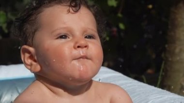 Charming curly child bathes in inflatable pool in the backyard