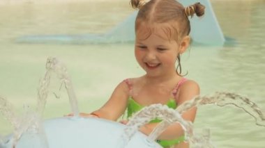 Little cute girl knocks on streams of water flowing from a fountain