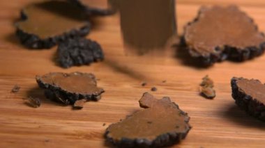 Slices of a black truffle mushroom are bouncing on the wooden board