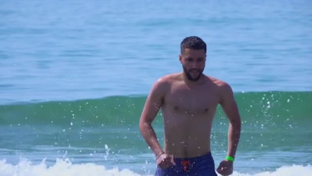 Mladý pohledný muž běží z vln mořského příboje — Stock video