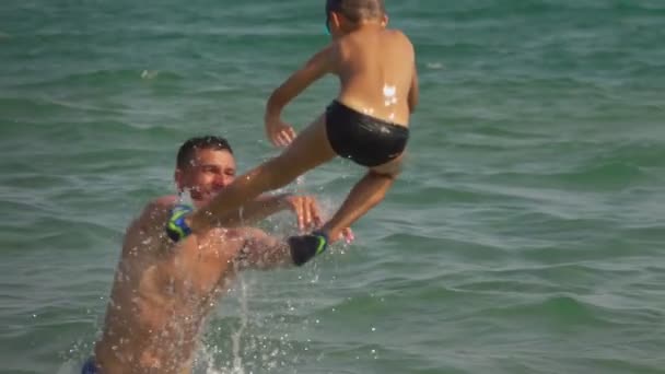 Joven papá lanza chico en agua de mar con salpicadura — Vídeo de stock