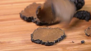 Several slices of a black truffle mushroom are falling on the board