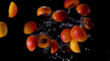 Juicy apricot halves are flying up with a water splashes on a black background