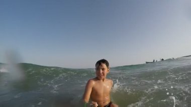 Boy is running backward and falling into the sea wave