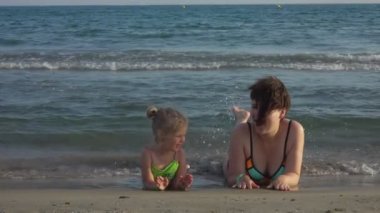 Mom and daughter lie on their stomach on the seashore and dangling feet