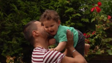 Handsome dad in a striped T-shirt plays with a curly baby boy outdoors